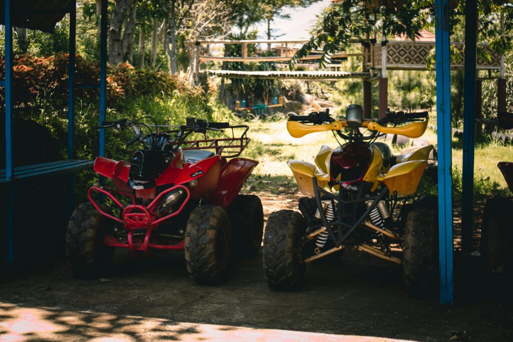 Two quad bikes parked under a shaded area surrounded by lush greenery.